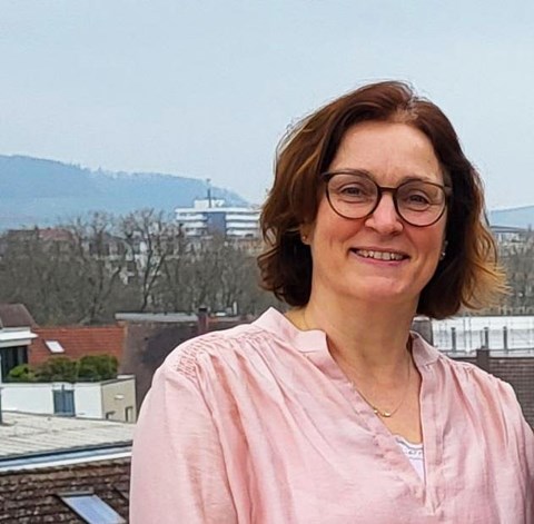 Portrait einer Frau, im Hintergrund befinden sich Häuser und Bäume